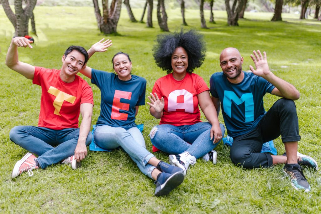 Happy 4-member T.E.A.M. sitting in the grass with tee shirts